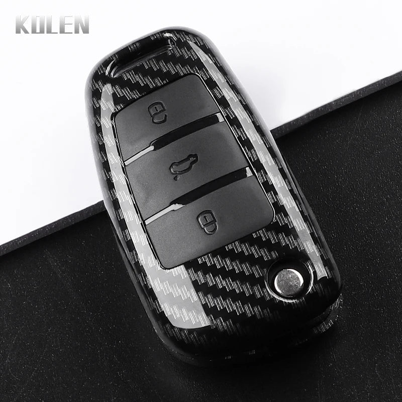 A black carbon fiber car key case cover with three visible key slots resting on a dark surface.