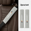 Two gray shoulder pads for a car seat belt set against a brown leather seat.