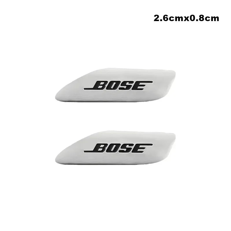 A white, elongated 3D aluminum car audio emblem with the brand name BOSE engraved on it.