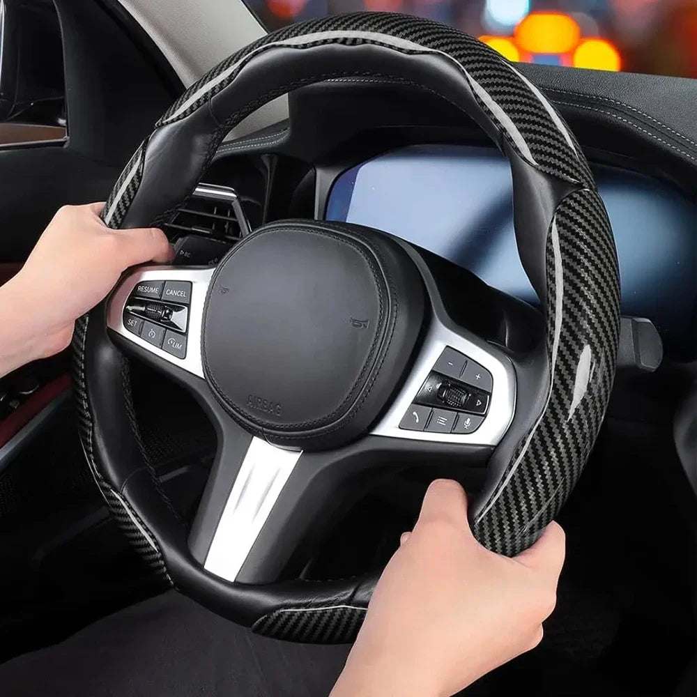 A hand grips a black carbon fiber steering wheel cover inside a car cockpit.