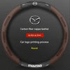 Housse de volant en cuir carbone marron avec logo Mazda argenté et texture ronde.