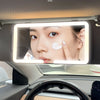A touch screen vanity mirror is mounted in a car interior, showing a close-up of a person's face.