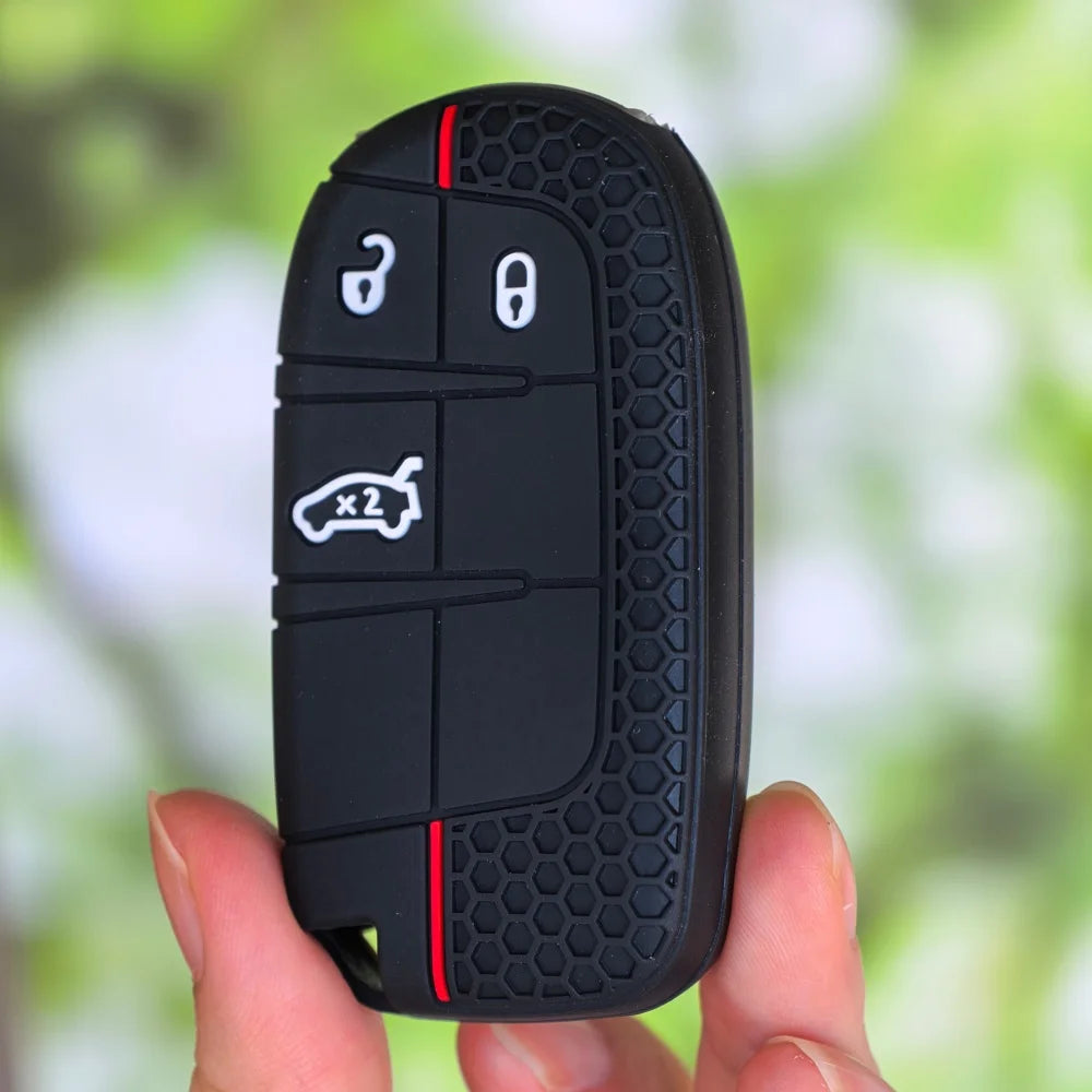 A hand holds a black silicone car key cover for Jeep, Dodge, and Chrysler models with various key cutouts visible.