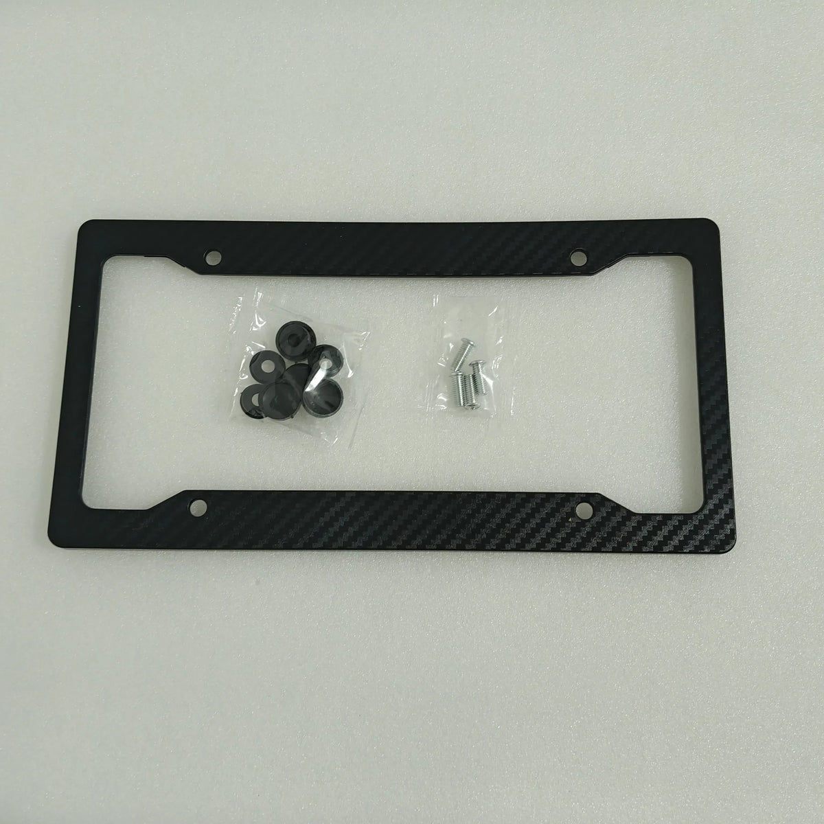 Black carbon fiber license plate frame with mounting hardware and small screws inside