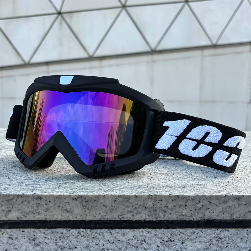 Black windproof sports goggles with iridescent purple and blue lenses resting on a gray stone surface.