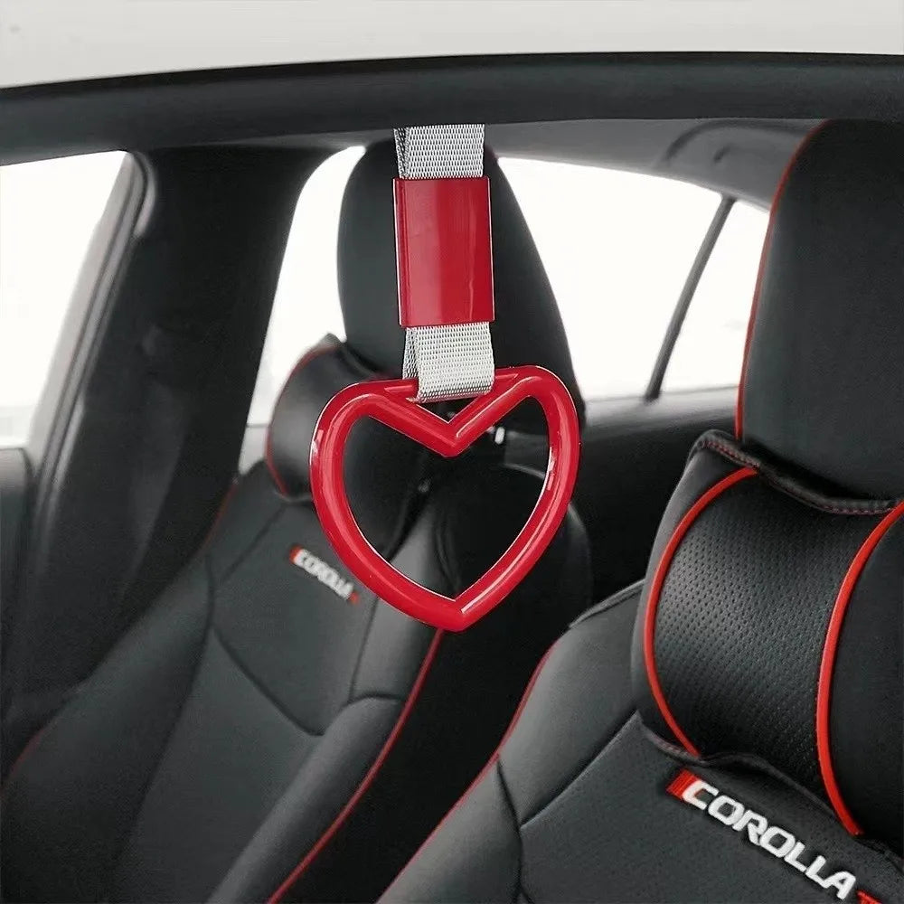 A red heart-shaped car handle accessory with a silver strap is shown inside a car interior.