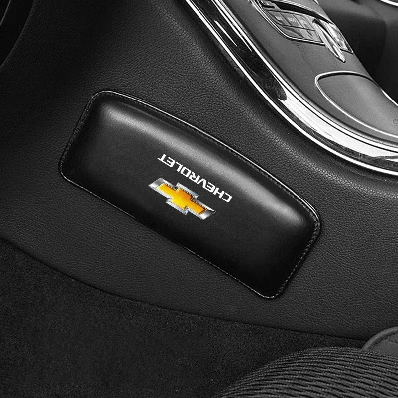 A black leather Chevrolet logo accessory is placed on a dark car interior surface.