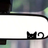 A close-up of a cat decal placed on a rearview mirror, showing a black silhouette of a cat against a white background.