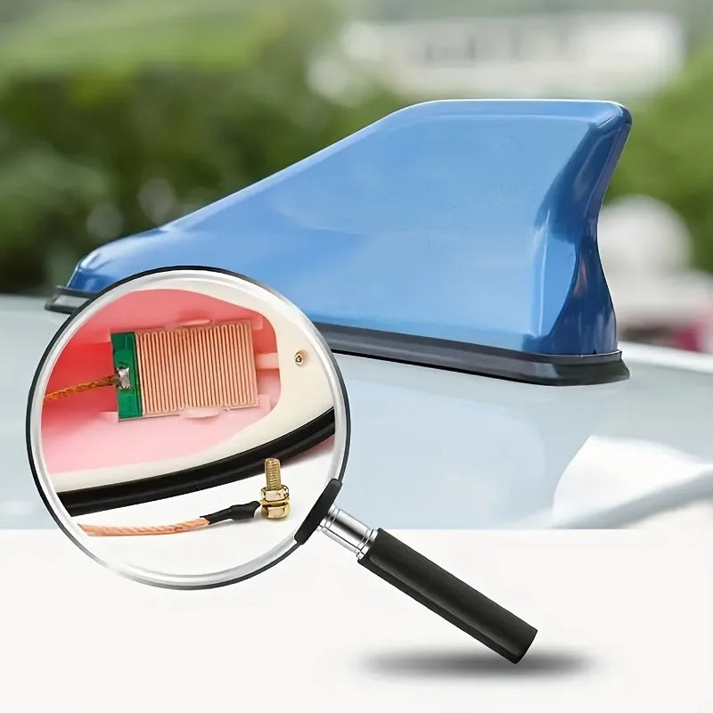 A magnifying glass shows the detail of a blue car antenna amplifier component.