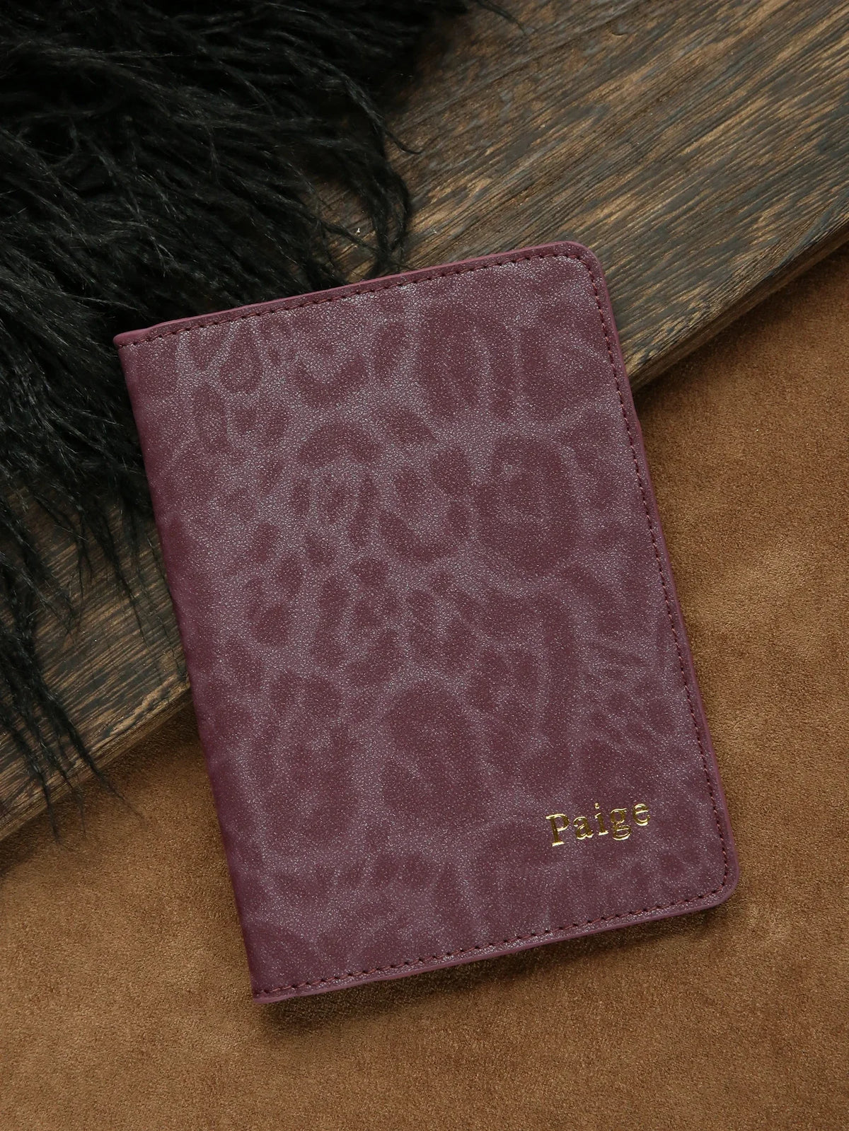 A deep purple leopard print passport holder resting on a brown surface next to black fur.