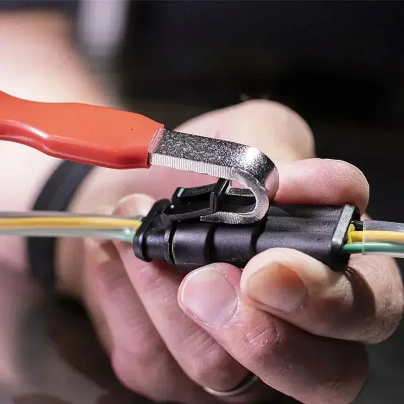 Eine Hand benutzt ein orange-silbernes Werkzeug, um einen schwarzen Elektrikerstecker zu trennen.