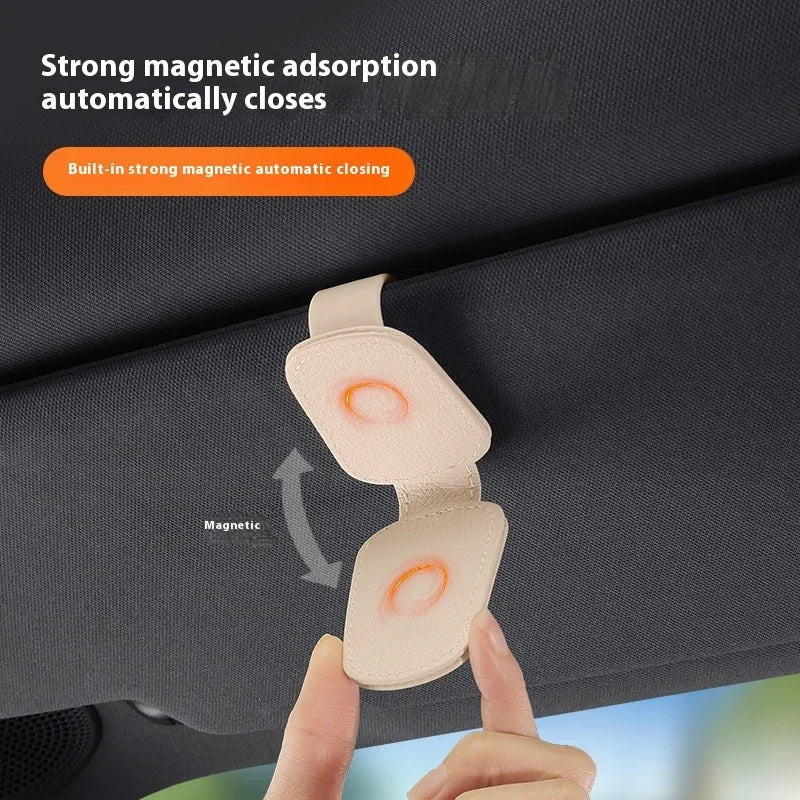 A hand is demonstrating a magnetic leather sunglasses holder that automatically closes on a car sun visor.