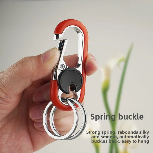 A hand holds a red spring buckle lock carabiner keychain with a silver ring.