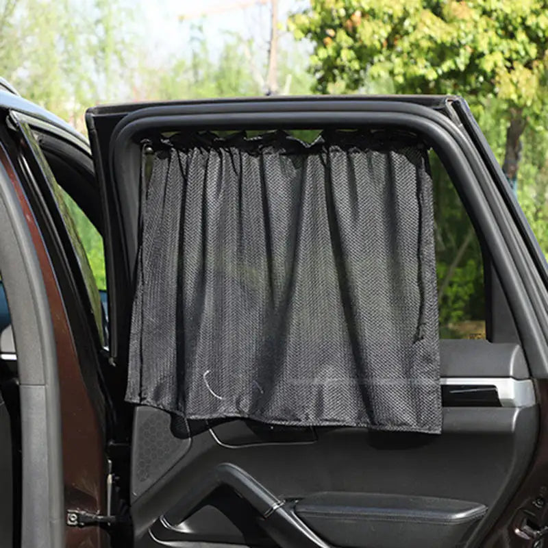 A black suction cup window sunshade is installed in the open window of a car.