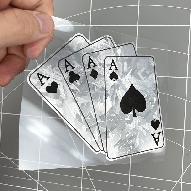A hand holds a stack of silver poker themed playing cards with aces and other cards on a transparent sheet.