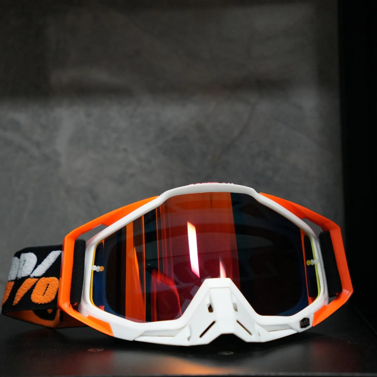 Orange and white high-performance motocross goggles resting on a dark surface.