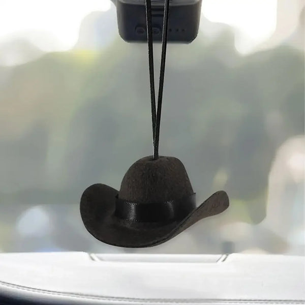 A black fabric cowboy hat ornament is hanging from a string against a blurred background.