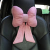 A pink bow knot fabric decoration is tied on a black car neck pillow.