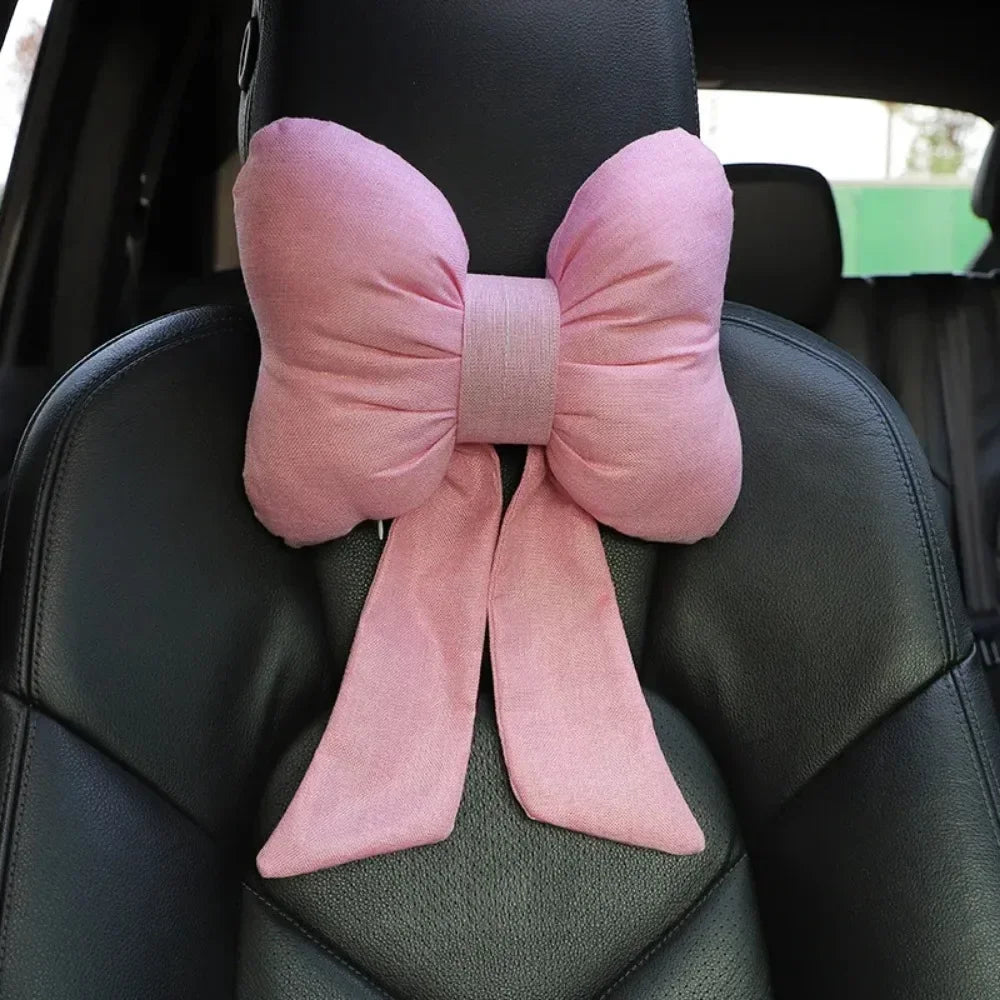 A pink bow knot fabric decoration is tied on a black car neck pillow.