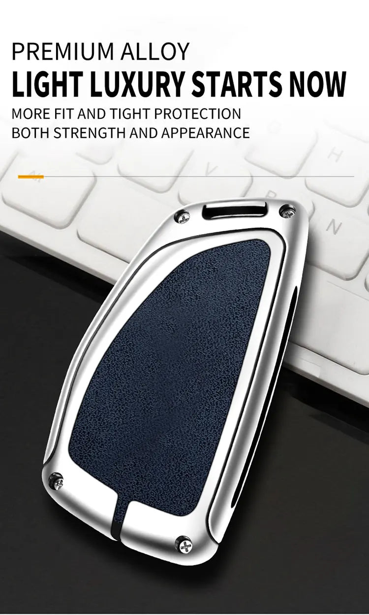 A silver car key case with a dark blue textured insert is shown resting on a white keyboard.