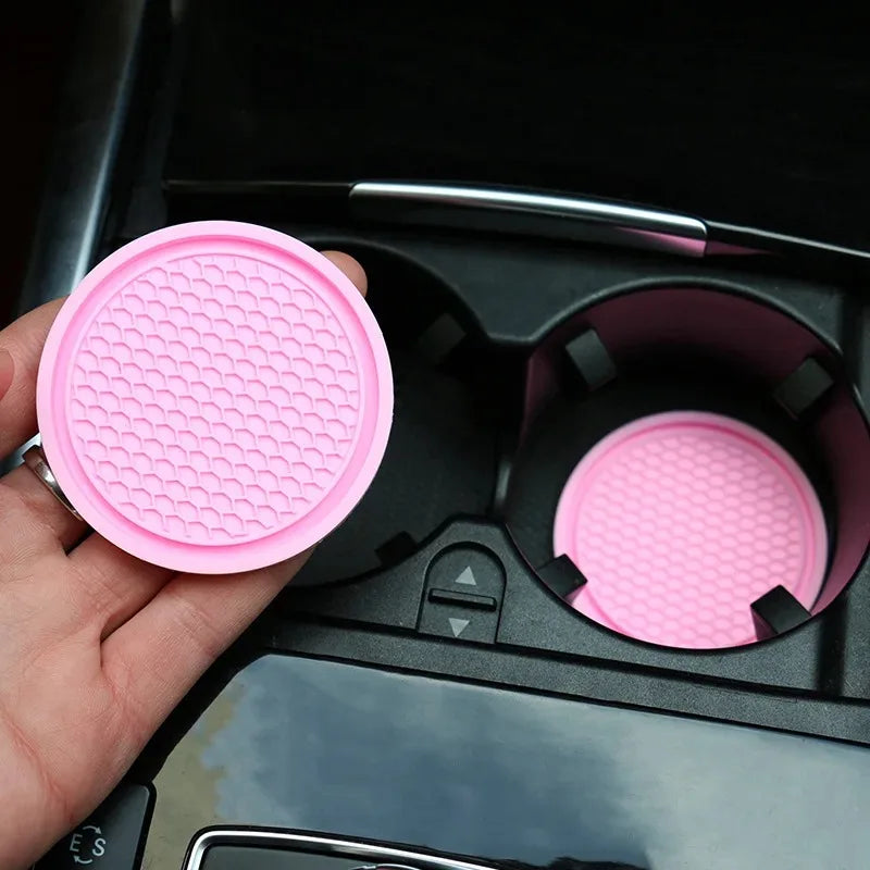 A hand holds a pink silicone car coaster, showing the texture and design of the product.