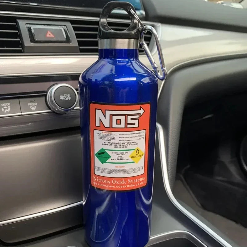 A blue insulated stainless steel travel kettle with a metal lid is placed in a car interior.
