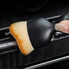 A black and natural colored curved silicone brush is shown being used on a car interior surface.