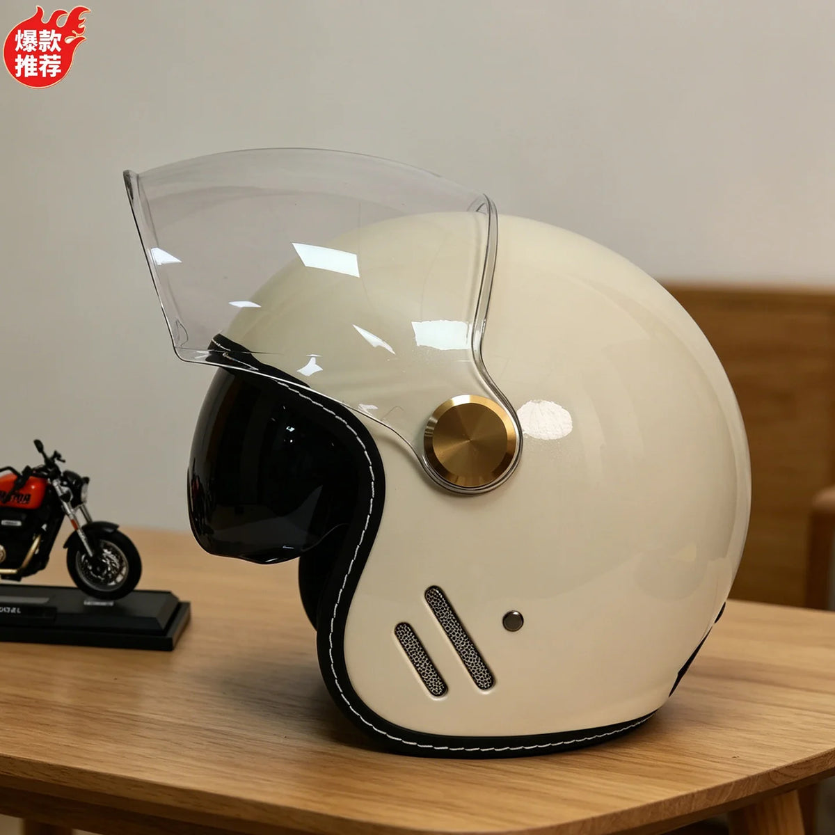 A cream-colored motorcycle helmet with a clear visor and gold accents resting on a wooden surface.