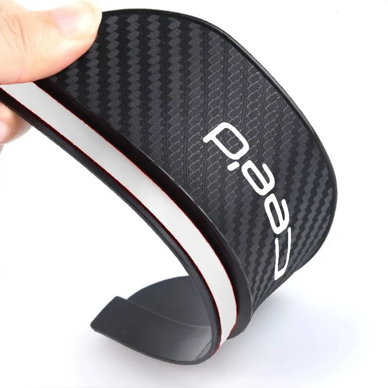 A black carbon fiber rain shield for a car rearview mirror is shown in profile.