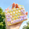 A hand holds a yellow keycap stress relief button set featuring various purple and yellow cartoon-themed buttons.