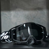 A pair of black high-performance motocross goggles resting on a dark surface.