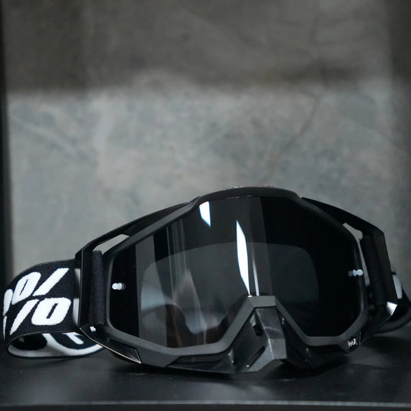 A pair of black high-performance motocross goggles resting on a dark surface.