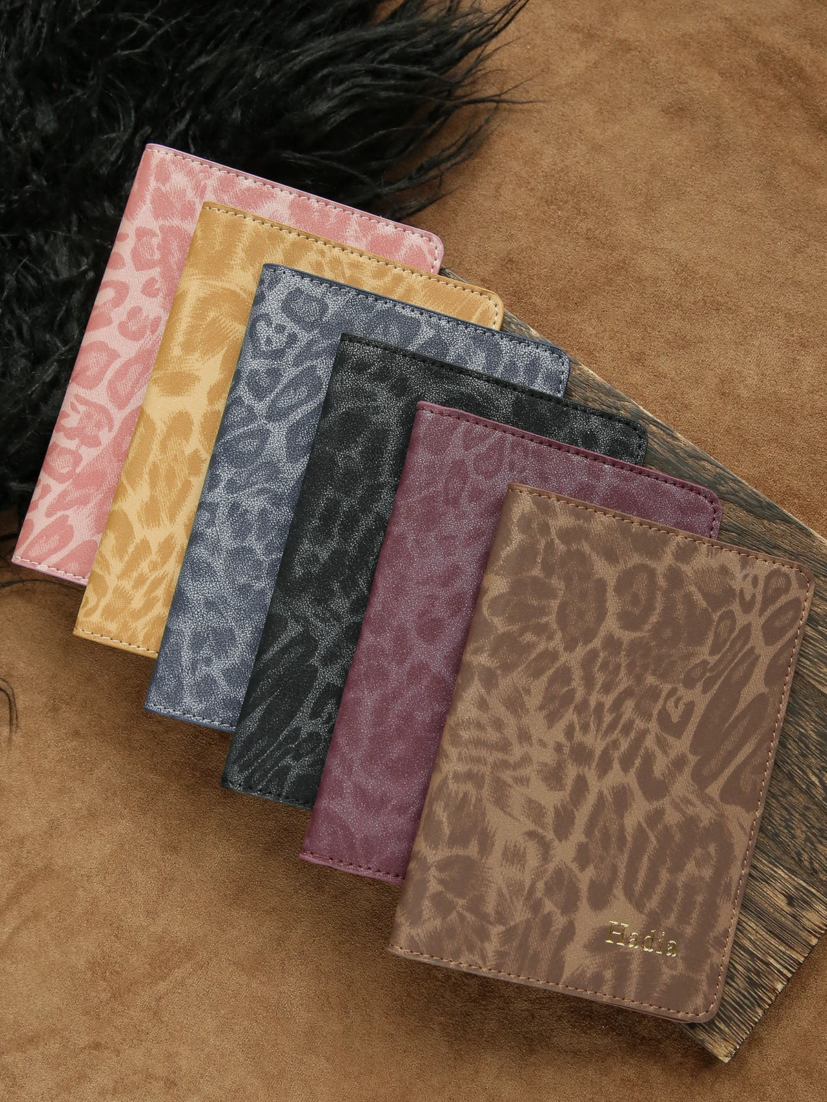 A collection of five leather passport holders in various leopard print colors laid on a brown suede surface.