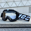 Black windproof sports goggles with a white and black strap resting on a gray stone surface.