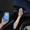 A hand is using a blue microfiber car wax applicator pad to polish the dark surface of a car.