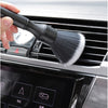 Une main tient une brosse de detailing noire à poils blancs, près de la grille d'un appareil de nettoyage intérieur automobil