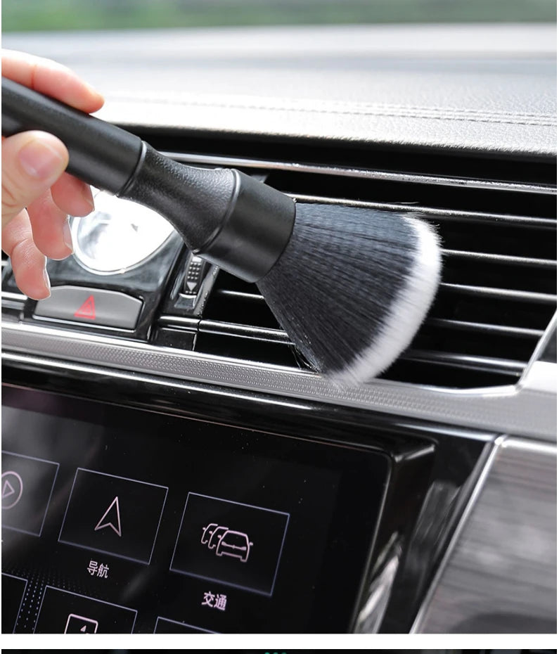 Une main tient une brosse de detailing noire à poils blancs, près de la grille d'un appareil de nettoyage intérieur automobil