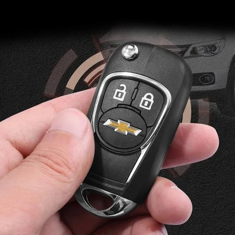 A hand holds a black key fob with a silver Chevrolet emblem and lock, against a dark background.