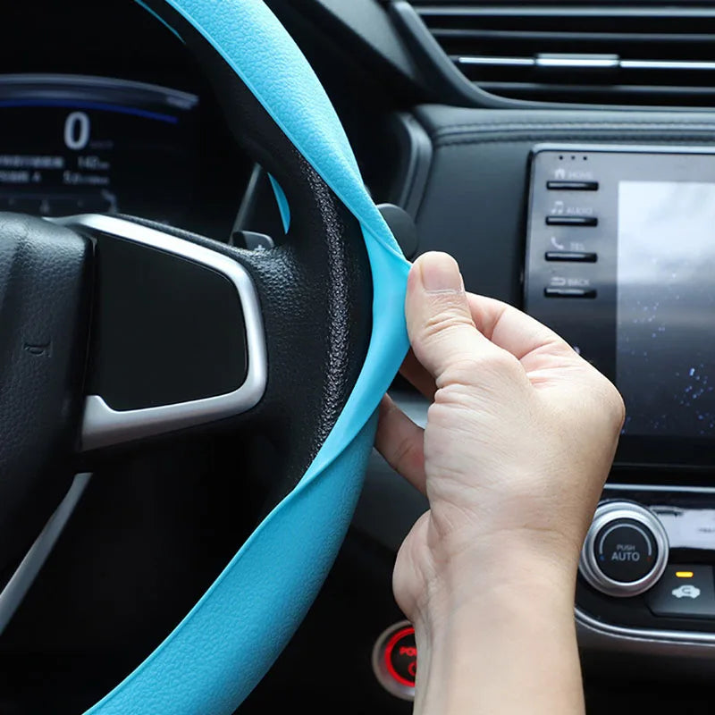 A hand is pulling a light blue silicone steering wheel cover onto the steering wheel of a car.