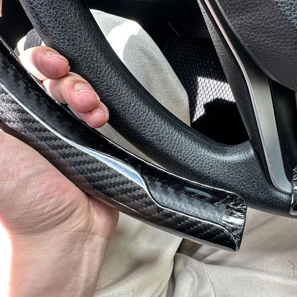 Eine Hand hält eine schwarze Kohlefaser-Lenkradabdeckung.