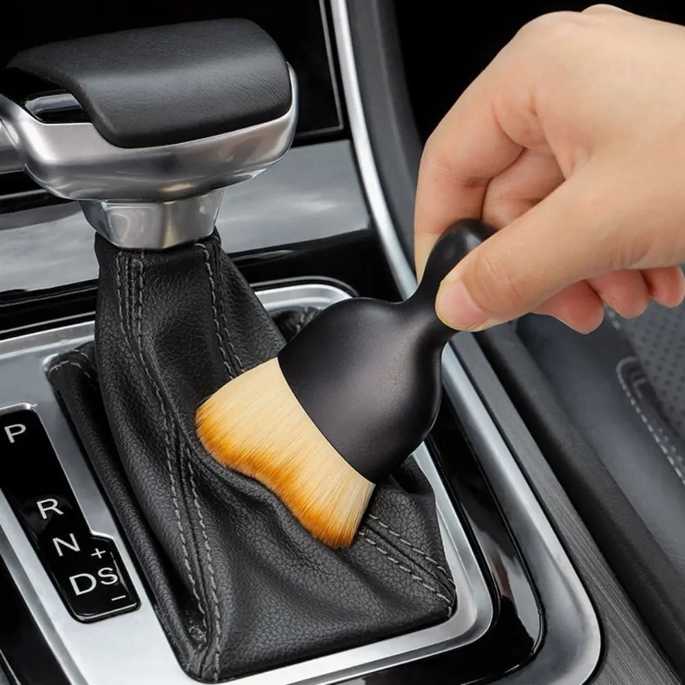 A hand is using a curved silicone cleaning brush to clean the interior of a car door panel.