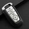 A silver multi-function key fob holder with several buttons resting on a dark textured surface.