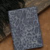 A dark blue leather passport holder with a leopard print pattern resting on a brown surface.