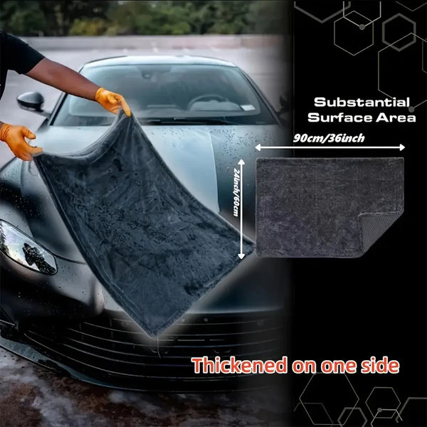 A black microfiber car drying towel is being used to wipe a car surface, highlighting its substantial area and thickness.
