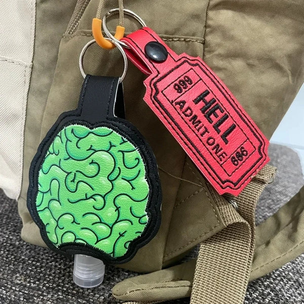 A red leather keyfob luggage tag with the name HELL and a green patterned charm attached to a tan canvas bag.