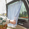 Una mano sostiene un parasol a cuadros azul y blanco para la ventana trasera de un coche.