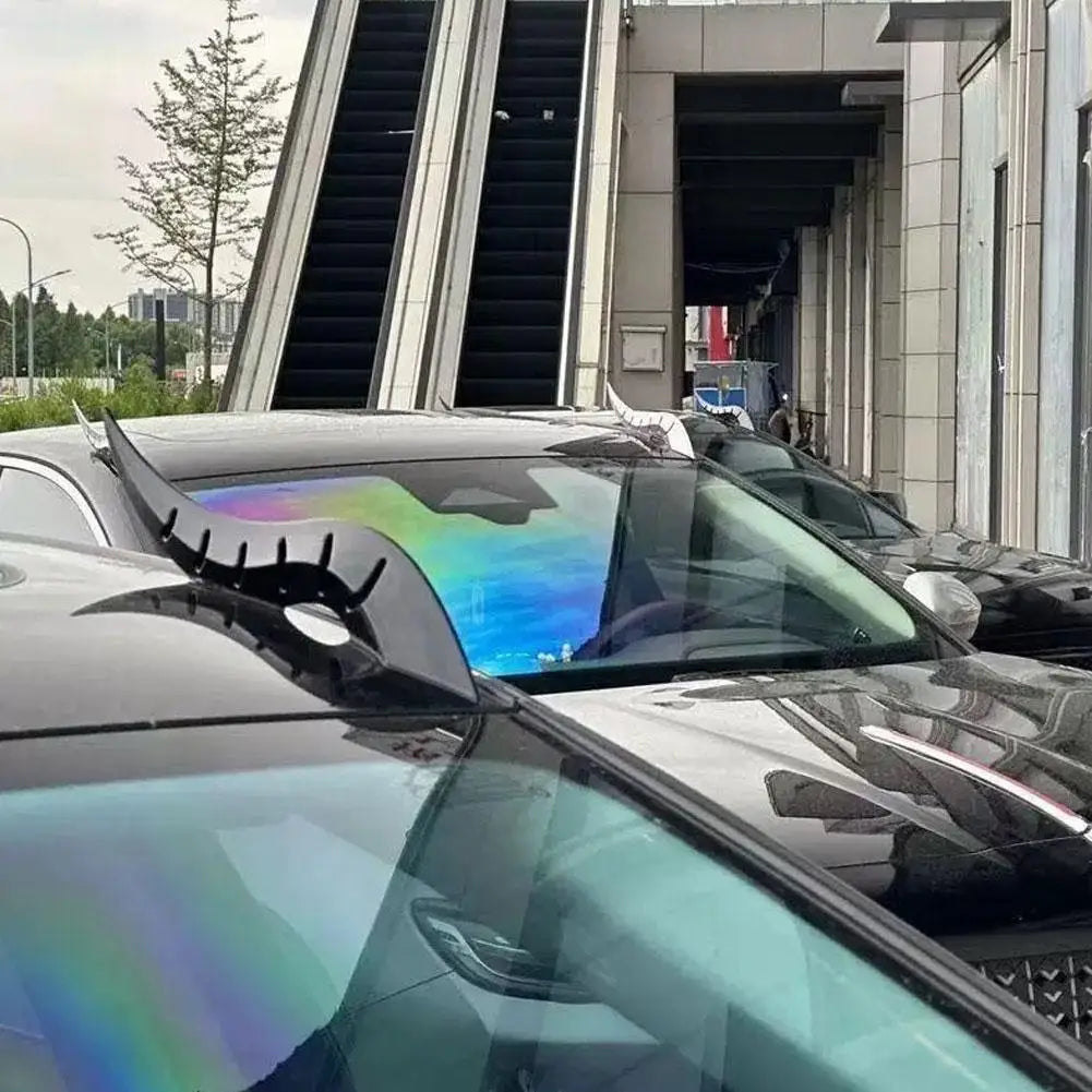 A close-up view of a black car roof decorated with iridescent, holographic vinyl featuring a fantasy dragon horn design.