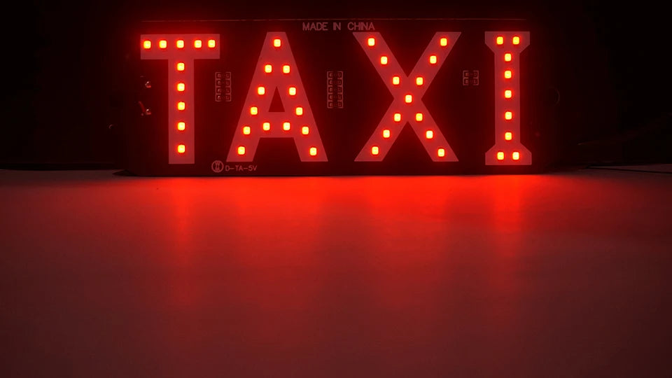 A close-up of an LED taxi indicator light sign displaying the word TAXI in bright red on a dark background.
