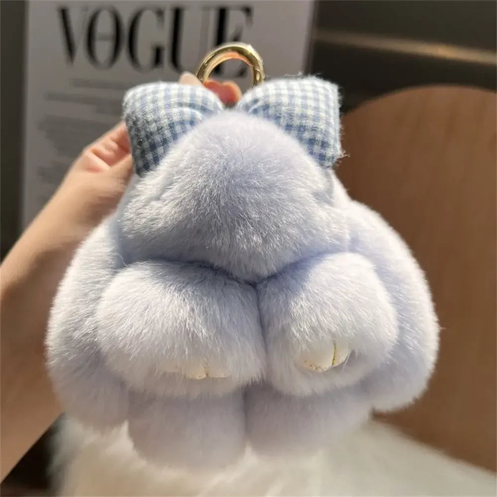 A light blue plush bunny keychain with soft fur and a gold ring is being held up.