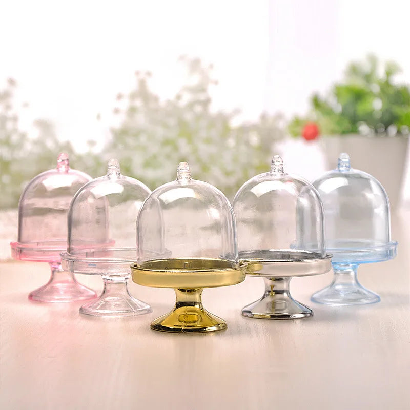 Eine Sammlung klarer Glas-Mini-Cupcake-Ständer in verschiedenen Formen und Farben auf einer weißen Oberfläche.